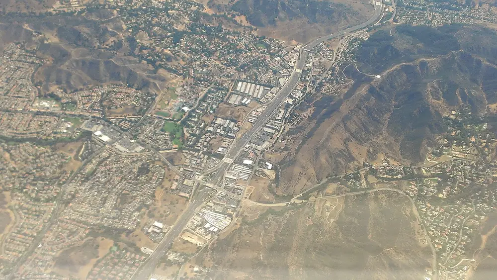 Aerial view of a freeway running through a hillside town with tracts climbing the slopes