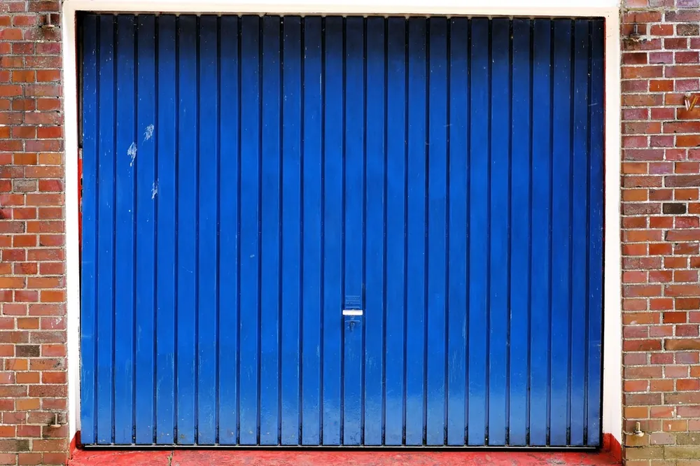 Blue vertical-ribbed steel garage door set in a red brick wall