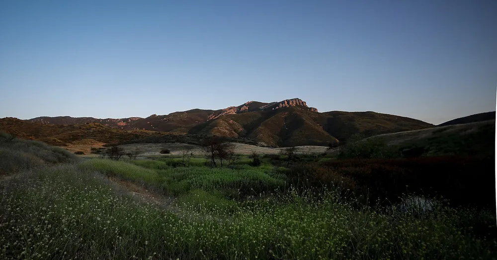 Green meadow at dusk below a rocky ridge line