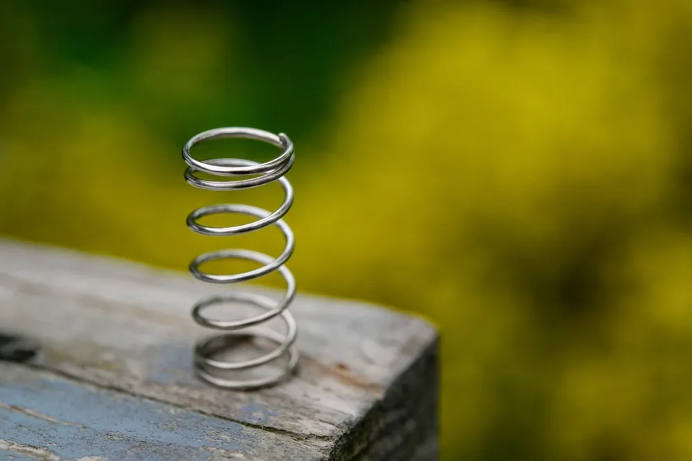 Small steel coil spring standing upright on a weathered wooden post