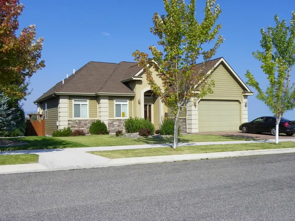 Two-story suburban house with a two-car garage and young trees along the street